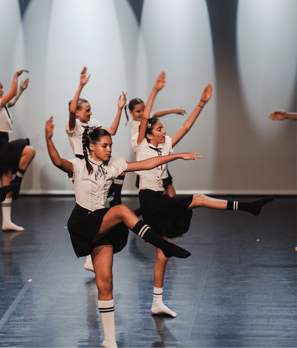 Danseuses en uniforme scolaire exécutant une chorégraphie sur scène.
