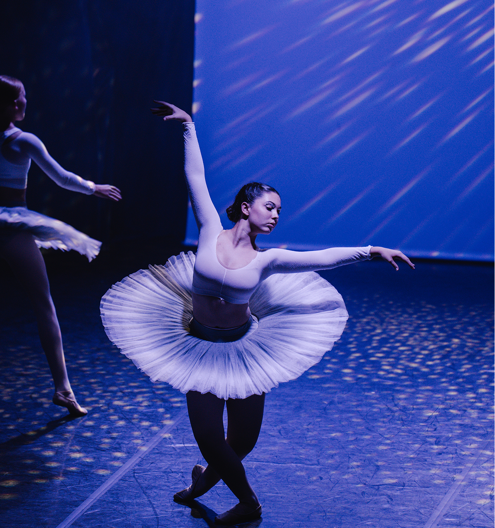 Danseuse de ballet en tutu blanc sur scène, éclairée par des lumières bleues.