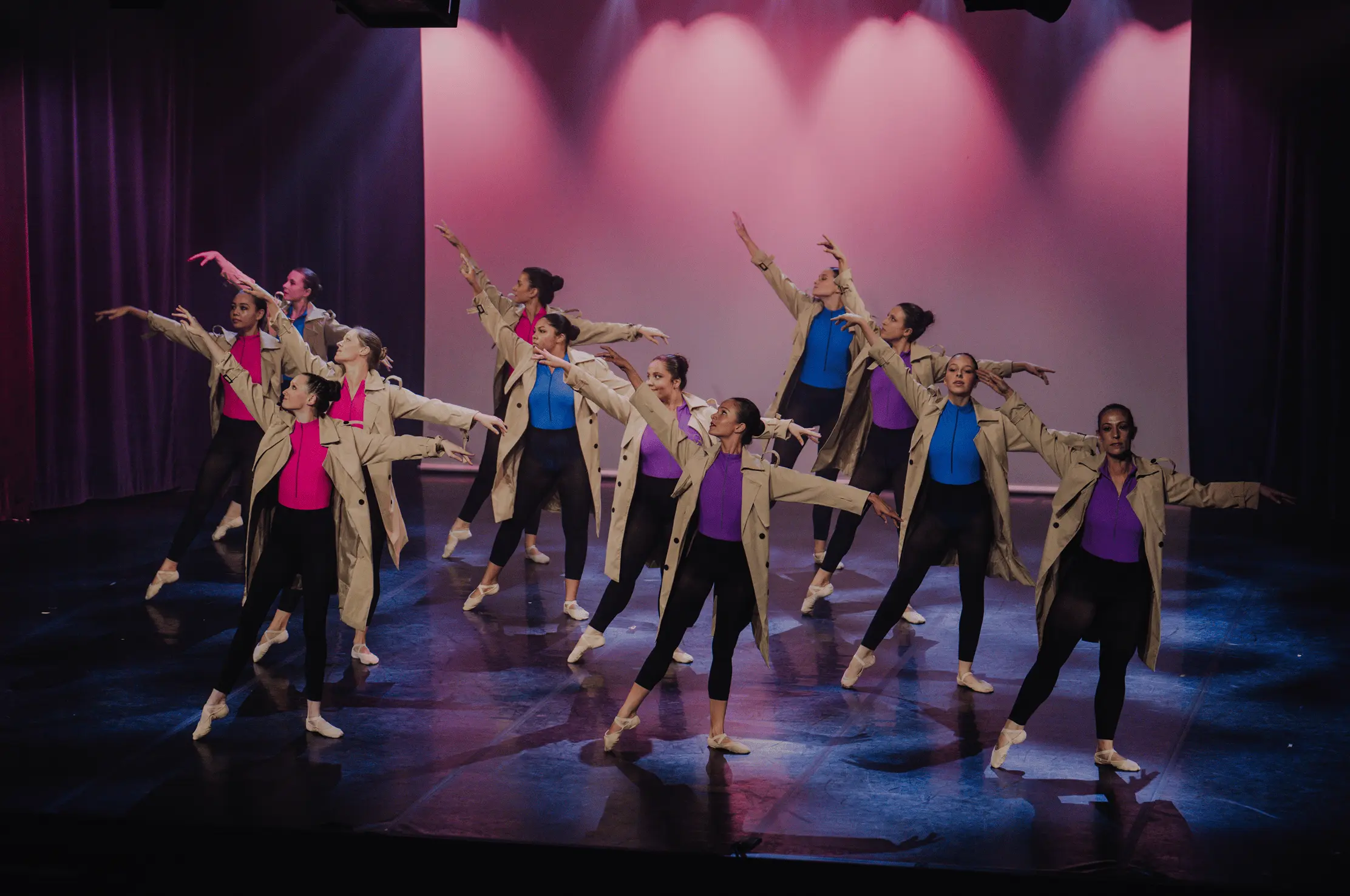 Danseurs en trench-coats sur scène, éclairage rose et violet.
